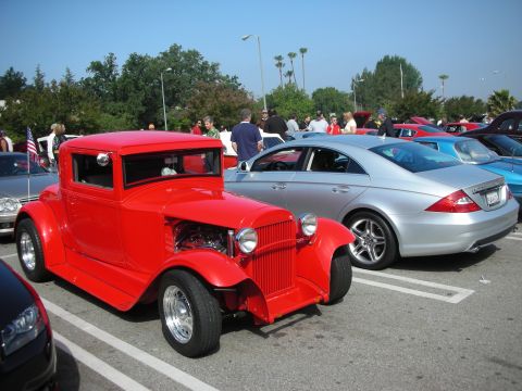 1998 Ford Crown Victoria - A red hot rod coupe and a silver sedan are parked at an outdoor car meet.