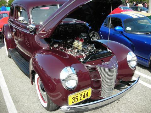 1998 Ford Crown Victoria - A classic maroon sedan with its hood open reveals a detailed engine, parked at an outdoor event.