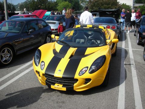 1998 Ford Crown Victoria - A yellow Lotus Elise with black stripes is parked at an outdoor event, with other cars and people around.