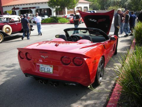 1998 Ford Crown Victoria - A red convertible Corvette C6 is parked on the street with its hood open, showing a checkered flag emblem.