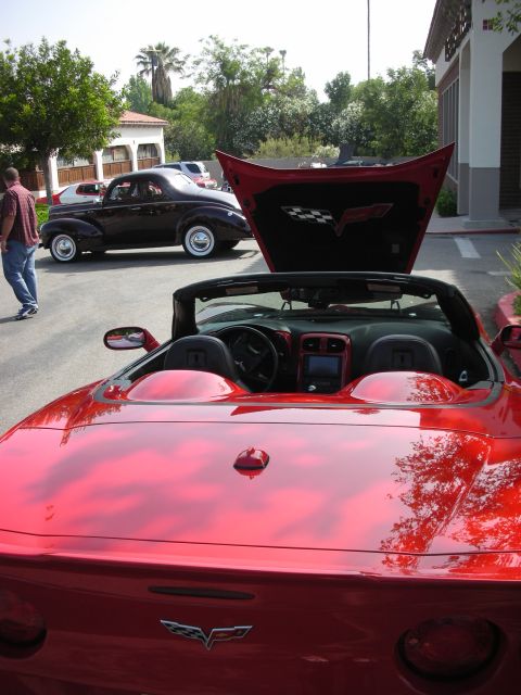 1998 Ford Crown Victoria - A red convertible sports car is parked next to a classic car, with its hood open revealing the Corvette emblem.