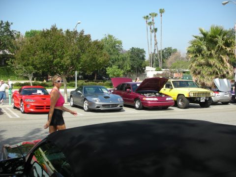 1998 Ford Crown Victoria - A red sports car is parked at an outdoor car show with other vehicles and people around.