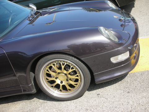 1998 Ford Crown Victoria - A dark purple car with gold wheels is parked on asphalt next to a yellow line.