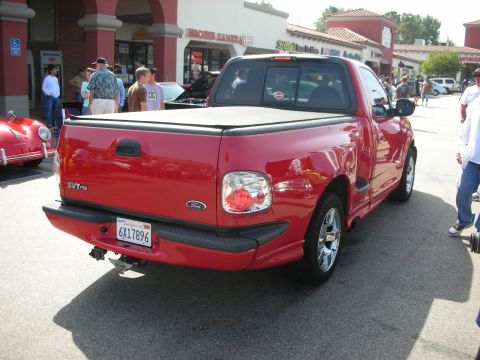1998 Ford Crown Victoria - A red Ford SVT Lightning pickup truck is parked in front of a shopping center with other vehicles and people around.