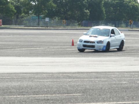 2001 Mercury Grand Marquis - A white Subaru WRX STI navigates a course marked by orange cones on a paved surface.