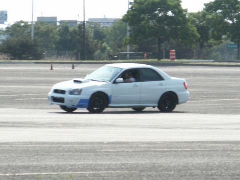 2001 Mercury Grand Marquis - A white sedan is captured in motion on an asphalt surface, with trees and buildings in the background.