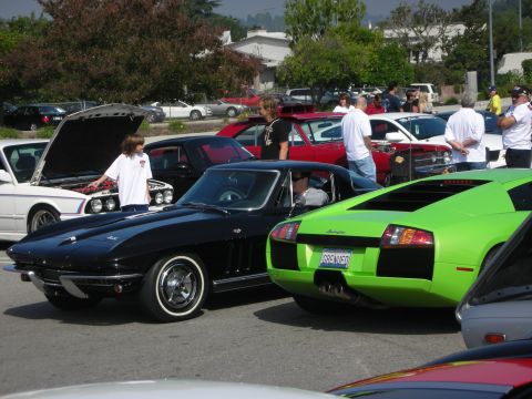 1998 Ford Crown Victoria - A black 1965 Corvette coupe with whitewall tires is parked at a car meet, surrounded by other vehicles.