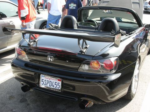 1998 Ford Crown Victoria - A black convertible sports car is parked at an outdoor event, showing its rear and a prominent spoiler.