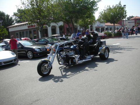 1998 Ford Crown Victoria - A custom-built trike with a prominent engine is seen at a car meet, alongside other vehicles.