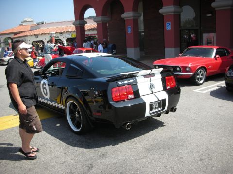 1998 Ford Crown Victoria - A black Shelby Mustang with racing stripes and the number 6 on the door is parked next to a red classic car.