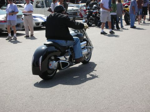 1998 Ford Crown Victoria - A black motorcycle with a rider is seen from behind at an outdoor gathering.