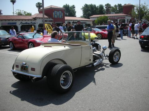 1998 Ford Crown Victoria - A cream-colored hot rod with exposed engine components and wide rear tires is parked among other vehicles at a car show.