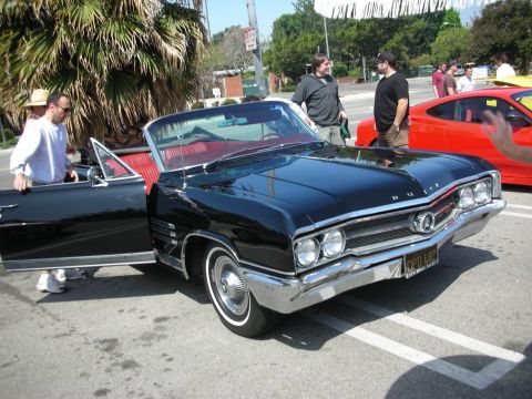 1998 Ford Crown Victoria - A classic black convertible with its door open is parked next to a red sports car.