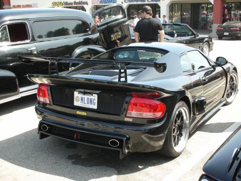1998 Ford Crown Victoria - A black sports car with a prominent rear spoiler and custom license plate is parked outdoors.