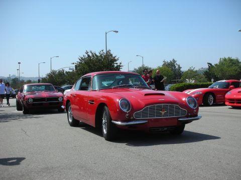 1998 Ford Crown Victoria - Several red cars are gathered on a sunny day, with a classic sports car in the foreground.