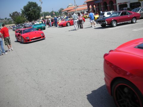 1998 Ford Crown Victoria - A red sports car is parked at an outdoor car meet, with other vehicles and people visible in the background.