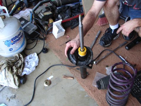1992 Ford Taurus - A person is shown disassembling a car's strut assembly in a garage setting with various tools and parts visible.