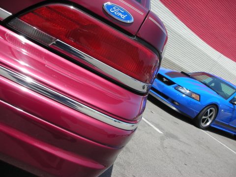 1998 Ford Crown Victoria - A red 1998 Ford Crown Victoria is parked next to a blue Ford Mustang.