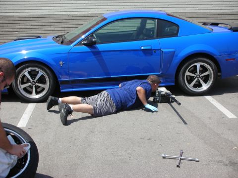 1998 Ford Crown Victoria - Man works on changing the tire of a blue Ford Mustang.