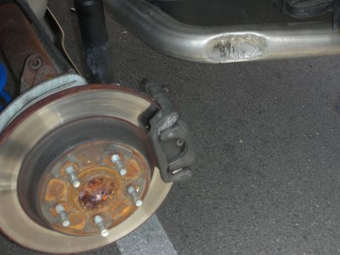 1998 Ford Crown Victoria - Close-up view of a vehicle's rear brake rotor and a damaged exhaust pipe.