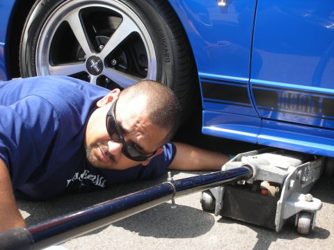 1998 Ford Crown Victoria - A man works on a blue Ford Mustang Mach 1, using a floor jack to lift the vehicle.