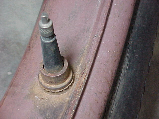 Close-up of valve stem and knurled metal cap on a rusty maroon-painted wheel rim with black tire edge visible