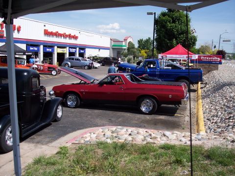 1972 Ford Ranchero - A red pickup truck is parked with its hood open at an outdoor event, with other vehicles and a service building visible.