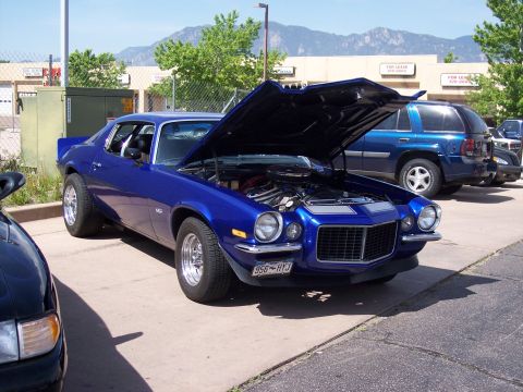 1972 Ford Ranchero - A bright blue 1970s muscle car is parked with its hood open, revealing the engine bay. Another vehicle is partially visible in the foregrou…