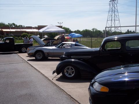 1972 Ford Ranchero - A line of cars, including a silver sports car and a black vintage vehicle, are parked at an outdoor event.