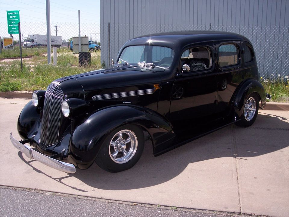 1936 black sedan hot rod with chrome bumpers and custom wheels parked on concrete