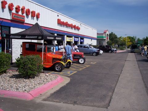 1972 Ford Ranchero - Cars are parked outside a Firestone store during an event. The orange hot rod in front has flames painted on it.