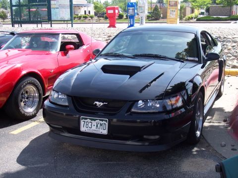 1972 Ford Ranchero - Black Ford Mustang parked next to a red Chevrolet Corvette at an outdoor event.