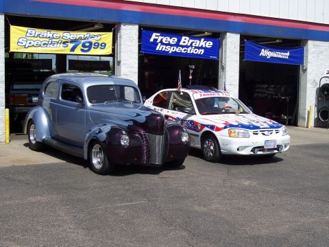 1972 Ford Ranchero - Two cars are parked outside a service station, one a classic coupe and the other a modern sedan decorated with patriotic themes.
