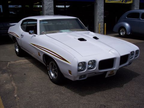 1972 Ford Ranchero - A white 1970s muscle car is parked in front of a building with another car visible in the background.
