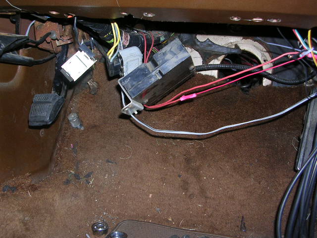 Brown carpeted floor with exposed wiring, fuse box, and pedals