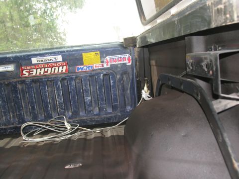 1978 Ford Bronco - The interior of a truck bed shows a blue tailgate covered in stickers and a coiled cable on the floor.