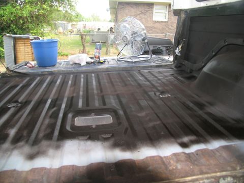 1978 Ford Bronco - The bed of a pickup truck is being prepped for coating, with a fan and supplies nearby.