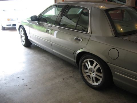 2001 Ford Crown Victoria - A gray 2001 Ford Crown Victoria is seen from the side, parked next to another vehicle in a garage.