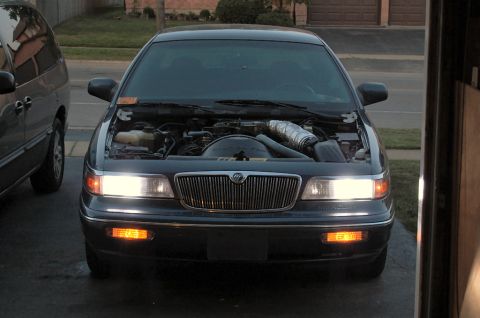 1985 Mercury Grand Marquis - The front of a Mercury Grand Marquis is shown with its hood up, parked next to a minivan.