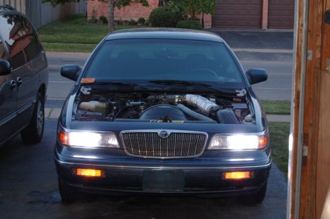 1985 Mercury Grand Marquis - Front view of a dark blue sedan with its hood open, parked next to a minivan.