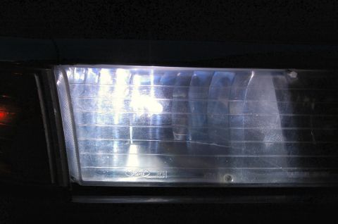 1985 Mercury Grand Marquis - Headlight assembly with visible Ford logo and horizontal fluting on the lens.