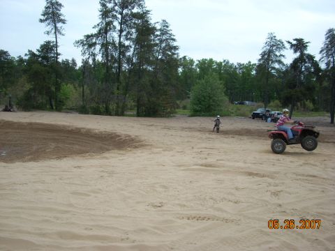 2000 Chevrolet Tahoe - An ATV rider catches air while a dirt bike rider is visible in the distance on a sandy track.