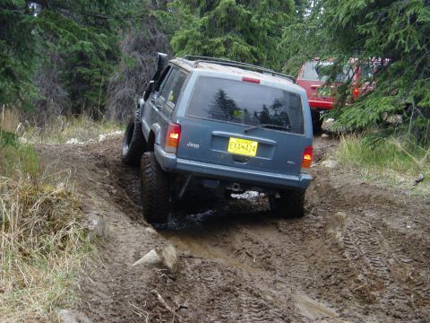 2000 Ford E350 - Jeep Cherokee XJ navigating a challenging muddy off-road trail with another Jeep following.