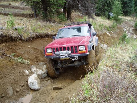 2000 Ford E350 - This Jeep Cherokee is tackling a challenging off-road course with mud and rocks.