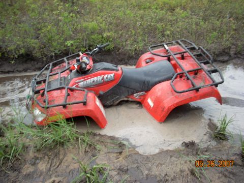 2000 Chevrolet Tahoe - An Arctic Cat ATV is stuck in a muddy puddle with grass growing around it.
