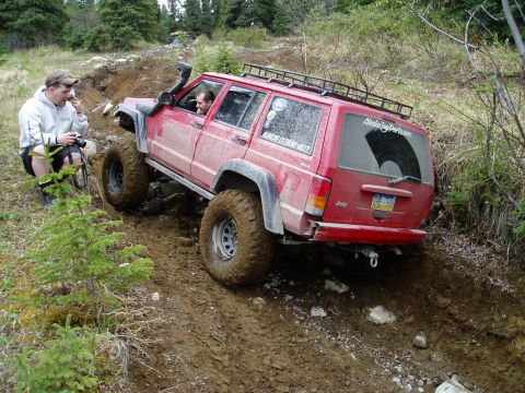 2000 Ford E350 - A red Jeep Cherokee navigates a steep, muddy trail with a person watching.