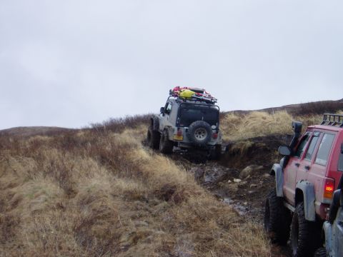 2000 Ford E350 - Off-road vehicles navigate a challenging muddy incline on a cloudy day.