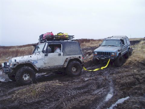2000 Ford E350 - Two Jeeps navigate a challenging muddy trail, one assisting the other with a tow strap.