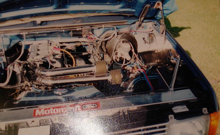 Engine bay of a blue car with chrome air pipes, brake booster and Motorcraft decal