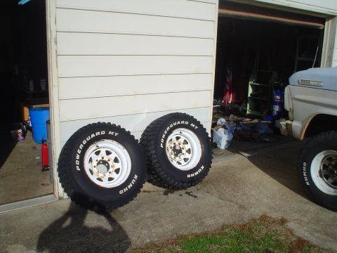 1967 Ford F-250 - Two off-road tires and a 1967 Ford F-250 truck are visible in front of a garage.